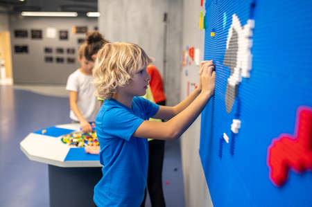 Profile of boy attaching lego piece to wall