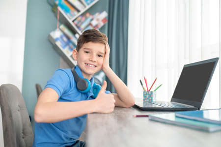 Joyous kid sitting in his room leaned on his desktop