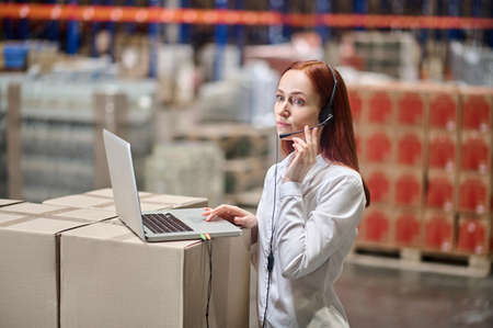 Woman in headset listening attentively standing near laptopの写真素材