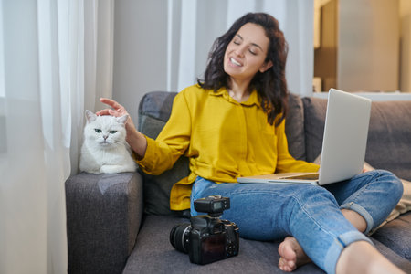 Cute young woman sitting on the sofa with her cat next to herの写真素材