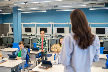 Woman looking at girl answering standing near deskの写真素材
