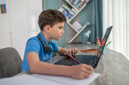Schoolboy seated at the desk staring at his laptop screenの写真素材