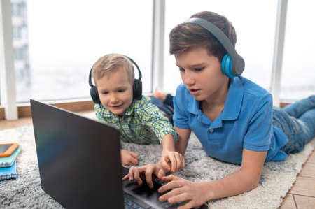 Siblings in headphones staring at the laptop on the floorの写真素材