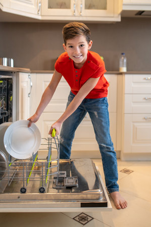 Smiling kid preparing dishes for cleaning in a dishwasherの写真素材