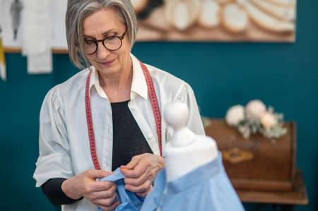 Woman standing near dummy touching blouse with pin