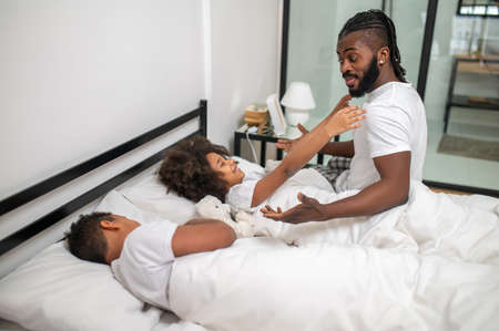 Man sitting on bed and lying girl stretching arms