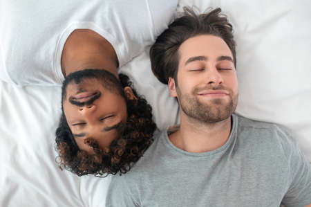 Young gay biracial couple sleeping in bedの写真素材