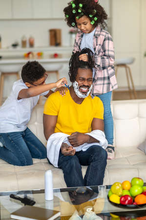 Boy shaving his laughing dad and girl braiding