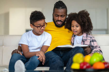 Dad reading book to children sitting on sofaの写真素材