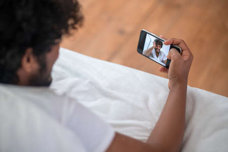 Curly-haired guy photographing himself with his cellphoneの写真素材