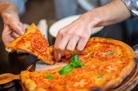 Close up picture of mans hands taking a slice of pizza