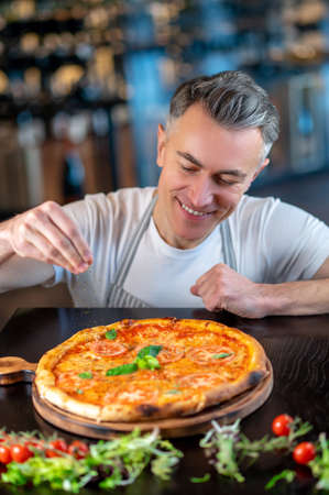 A chef making topping on a italian pizza