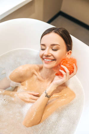 Smiling cheerful female bathing in a bathtub