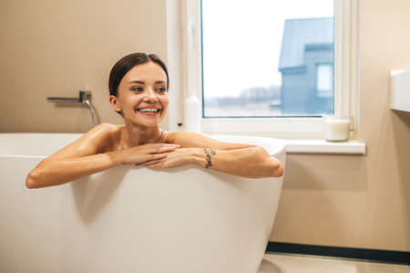 Happy young female sitting in the bathtub