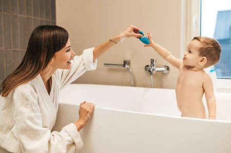 Merry female parent playing with her child in the bathroom