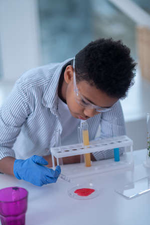 A dark-haired boy in a lab coat looking busy while doing chemical experiment