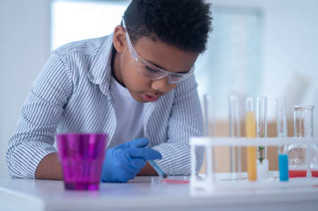 A dark-haired boy in a lab coat holding a syringe with a reagent and looking busy