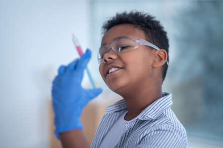 A smiling boy in protective eyeglasses holding a syringe in handの写真素材