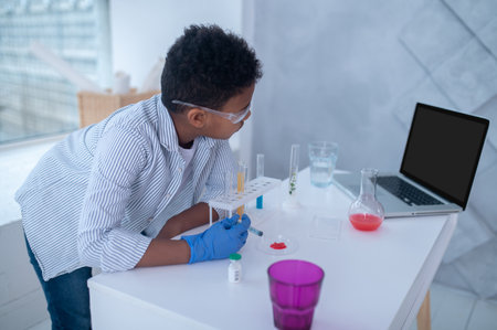 A dark-haired boy in a lab coat looking busy while doing chemical experimentの写真素材