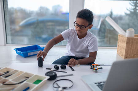 A cute teen sitting at the table and playing with toy wheels
