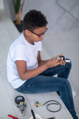 A dark-skinned boy in white tshirt and jeans playing with a toy transformerの写真素材