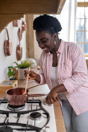 Contented african woman in pink clothes cooking in the kitchenの写真素材