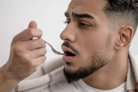 A sick man taking a spoon with medicineの写真素材