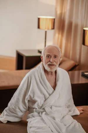 A gray-haired bearded man in a white robe in a hotel roomの写真素材
