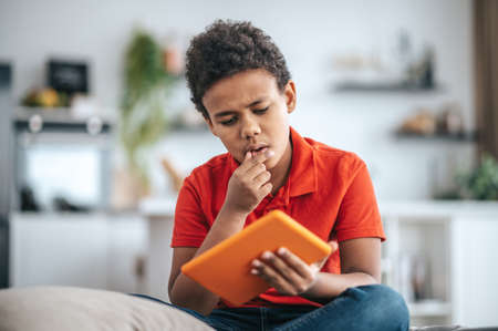 A boy holding a tablet and looking thoughfulの写真素材