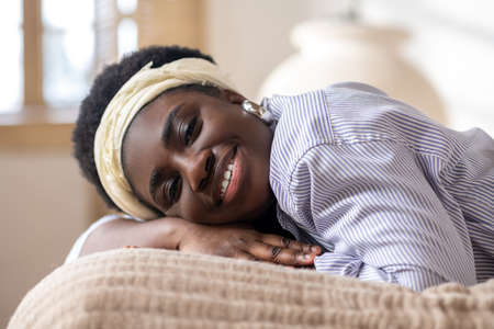 African american woman laying on bed and looking dreamyの写真素材