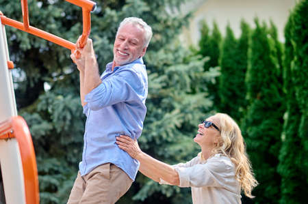 A gray-haired man hanging on horizontal bar at the sports ground
