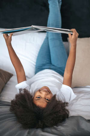 A girl lying on bed with her legs up and reading a magazineの写真素材