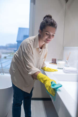 A young woman in yellow gloves cleaning the surfaces in the bathroom