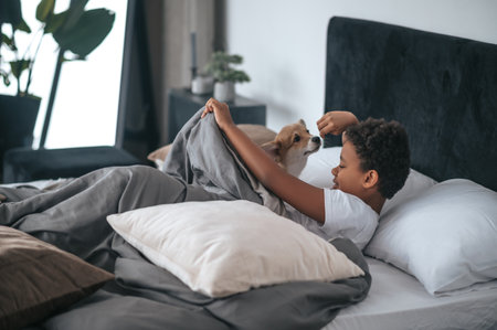 A boy laying in bed and a dog together with himの写真素材