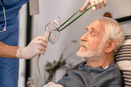 Medical worker preparing a bedridden aged man for oxygenationの写真素材