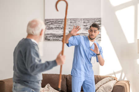 Aggressive patient brandishing his cane at a scared in-home nurseの写真素材
