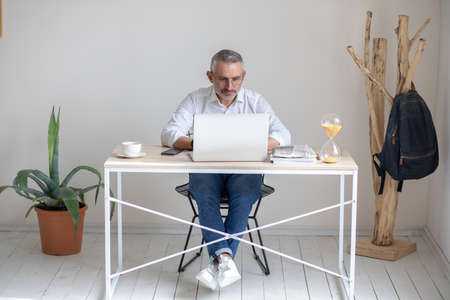 Man with glasses looking intently at laptop in officeの写真素材