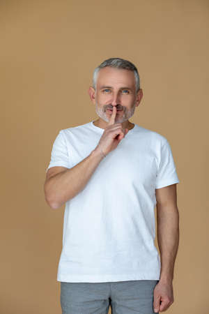 A gray-haired mid aged man showing a silence sign