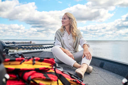 A blonde mature woman in white clothes sitting on a boat and looking dreamy