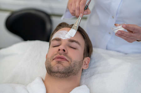 Cosmetologist applying cream on clients face with a brushの写真素材