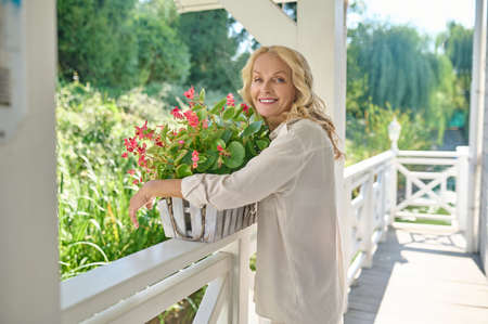 Pretty blonde woman in white with the flowers at her houseの写真素材