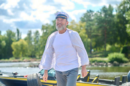 A bearded man in a captains cap looking contented