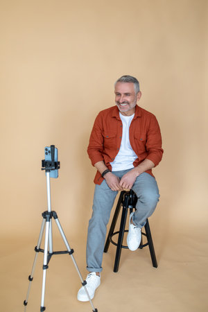 A man in a red jacket sitting on a stool in a studio and making selfieの写真素材