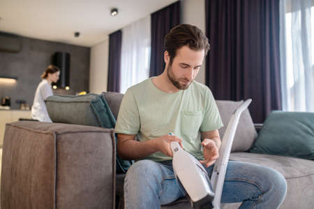 Man holding part of vacuum cleaner sitting on couchの写真素材