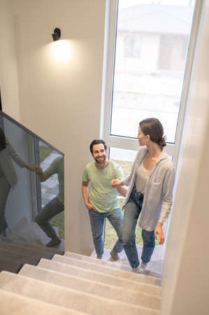 Woman climbing stairs turning around holding mans handの写真素材