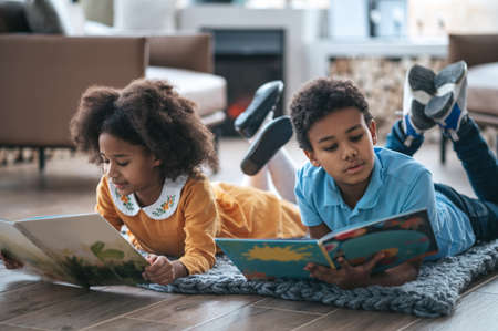 Two kids lying on the floor and reading a bookの写真素材
