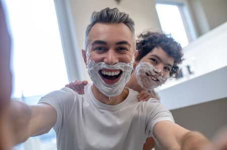 Dad and son looking funny with shaving foam on their facesの写真素材
