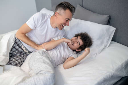 Father and son having fun in bed in the morning and looking joyfulの写真素材
