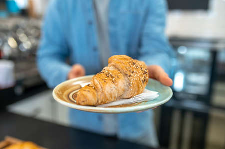 Male hands holding out croissant to camera