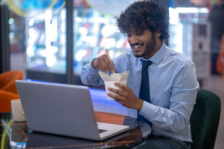 Man eating japanese food smiling at laptopの写真素材